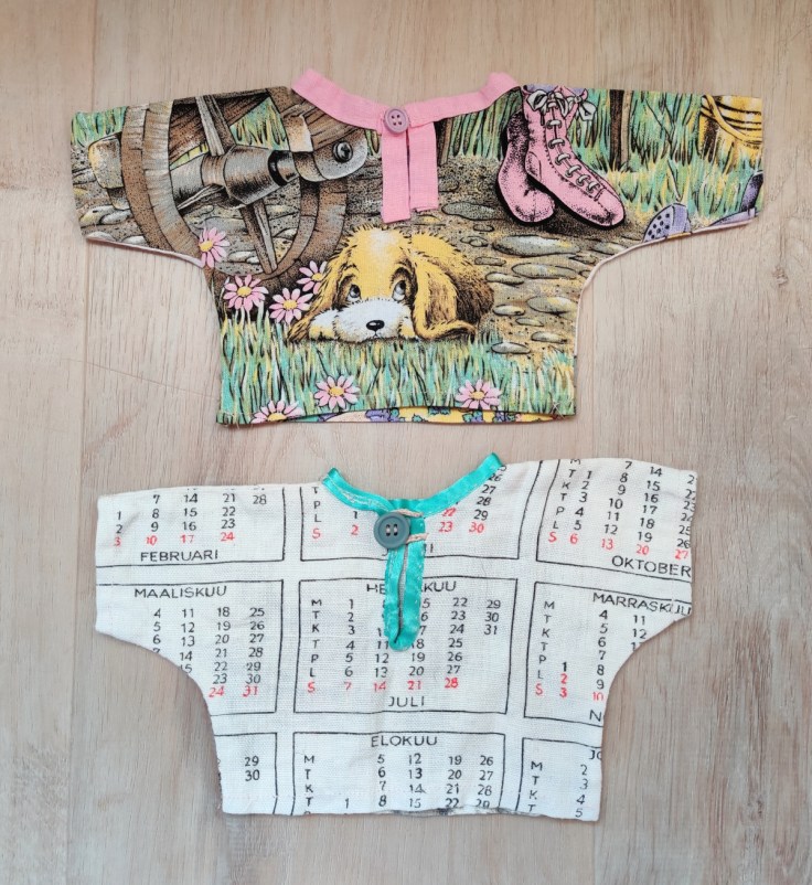 Two self-made doll shirts, seen from the back. The second shirt is made from a 1980's fabric calendar.