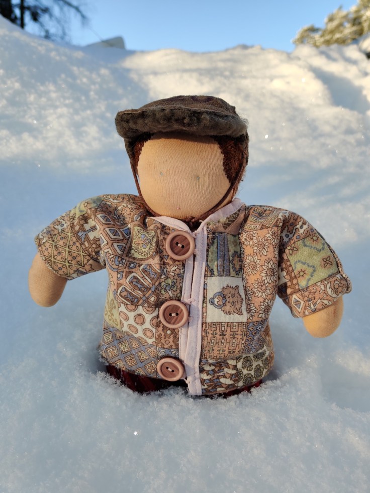A Steiner doll / Waldorf doll out in the snow wearing a homemade winter coat and hat.